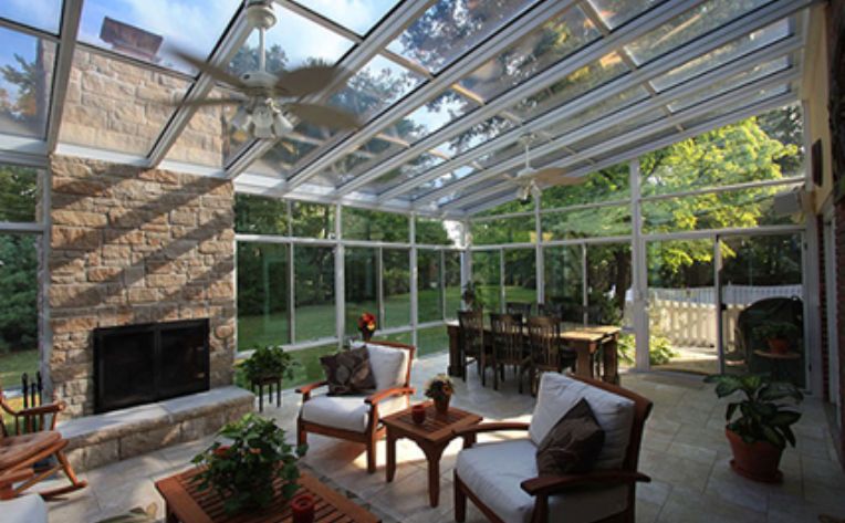Interior of a sunroom with a dining room table, outdoor chairs and a coffee table, and a fireplace with a ceiling fan overhead.